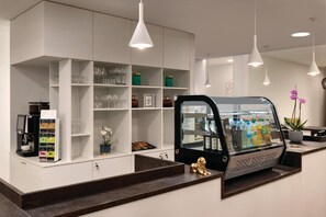 A modern bar area with a coffee machine, shelves with glasses, a refrigerator with beverages, and a gold lion statue.