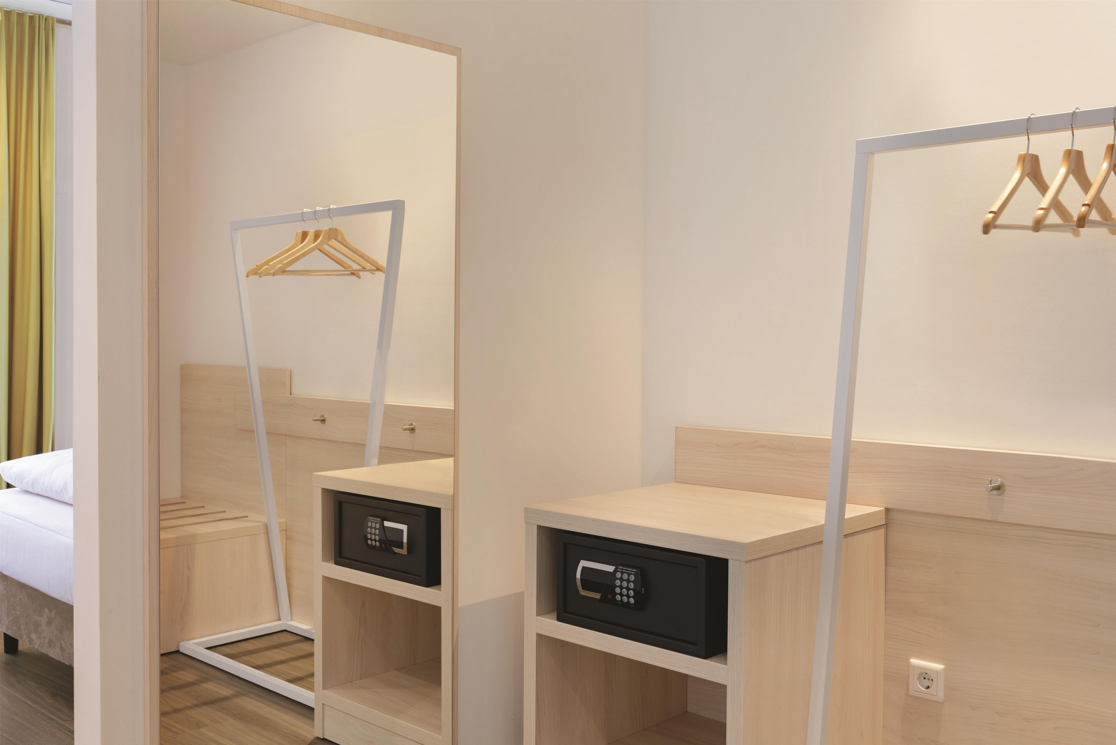 Ein Hotelzimmer mit Bett, Spiegel, Kleiderschrank und Nachttisch mit Bedienfeld.