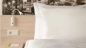 A hotel room with a bed, a nightstand, a wall-mounted lamp, and a power outlet. - Super 8 by Wyndham Augsburg (Augsburg)