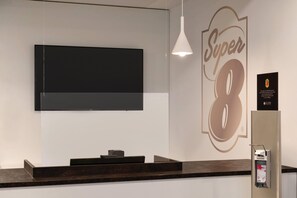 Una recepción con un televisor de pantalla plana montado encima, un cartel en la pared con el número '8', y un extintor a la derecha.