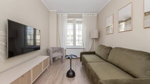 A modern living room with a flat-screen TV, a sofa, a chair, a small table, and a window with curtains.