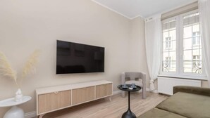 A modern living room with a flat-screen TV, a white console table, a round side table, a grey armchair, and a sofa.