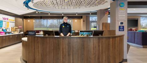 A hotel reception desk with a modern design, a digital display, and a view of the outside.