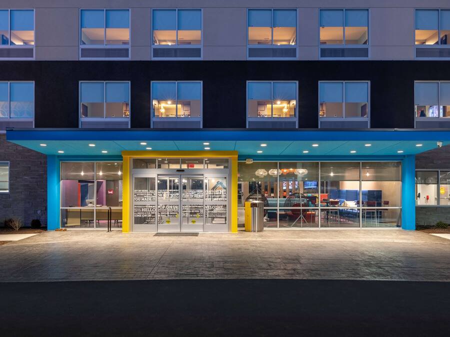 Een moderne hotelentree met glazen deuren, een blauw zonnescherm en een goed verlicht interieur zichtbaar door de ramen.