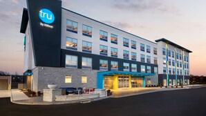 Een modern hotel met een opvallend 'tru by Hilton'-bord, een goed verlichte ingang en een strak, eigentijds ontwerp.
