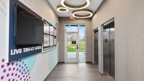 Een moderne lobby met een groot televisiescherm, een glazen deur en twee liften.