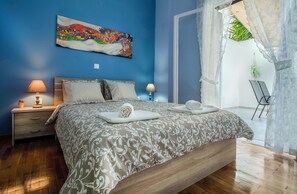 A bedroom with a bed, two bedside tables, a nightstand, a painting on the wall, and a view of the outdoors. - Elegant and renovated flat in Dafni (Dafni-Ymittos)