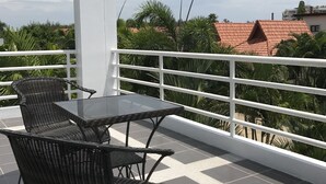 Un balcón con mesa y sillas, baranda blanca y vista a edificios y árboles.