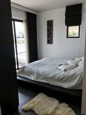 A bedroom with a bed, a window with curtains, a wall-mounted artwork, and a small rug.