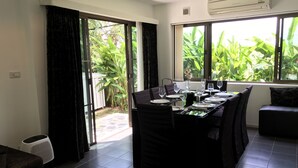 Un área de comedor con una mesa lista para cuatro personas, un sofá negro y ventanas grandes con vistas a zonas verdes.