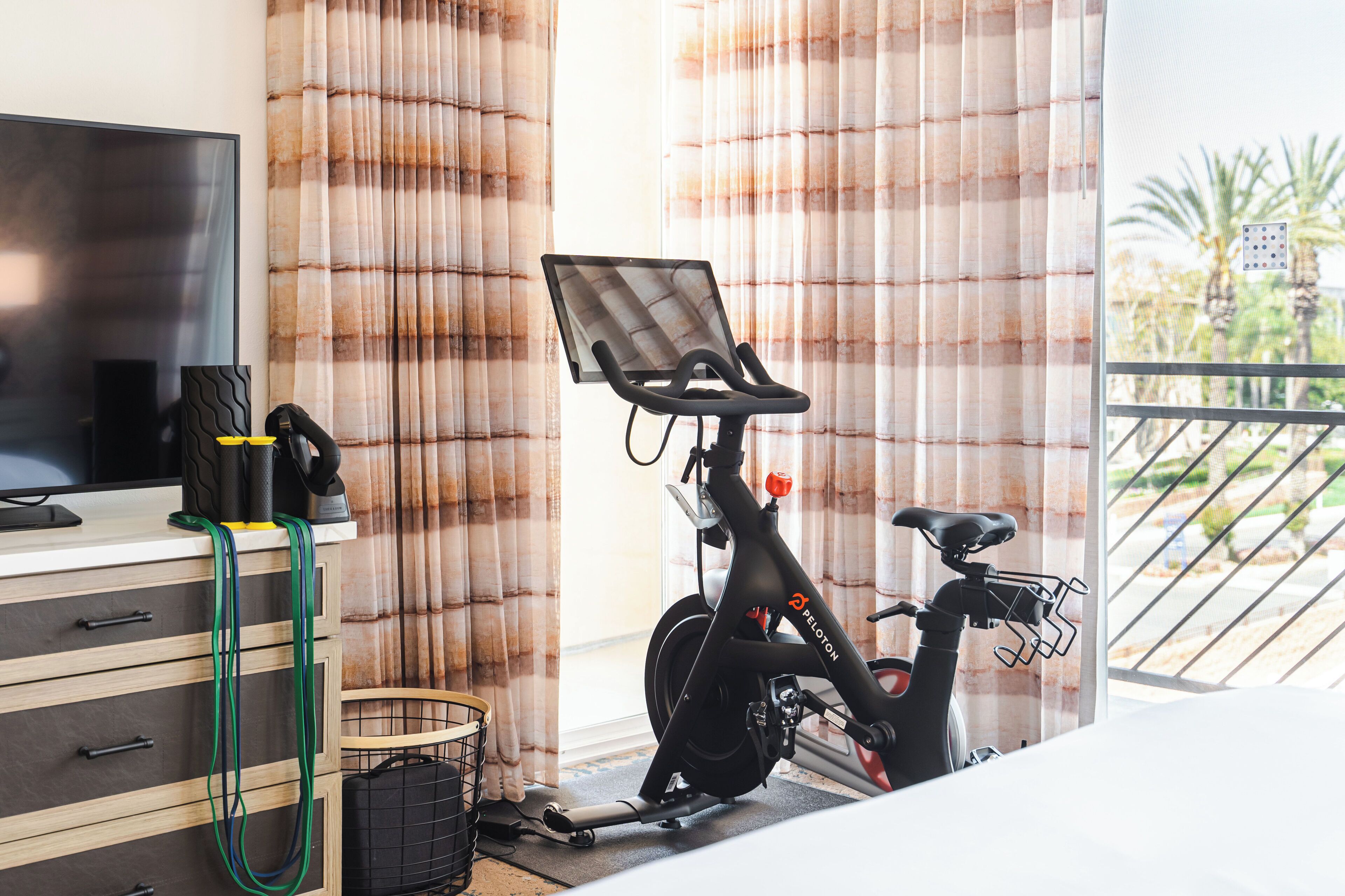 A room with a TV, a Peloton exercise bike, and a window with curtains.