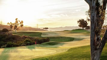 A golf course with rolling green hills, trees, and a clear sky.