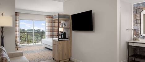 A hotel room with a bed, a TV, a wooden cabinet, and a balcony with a view of the outdoors.