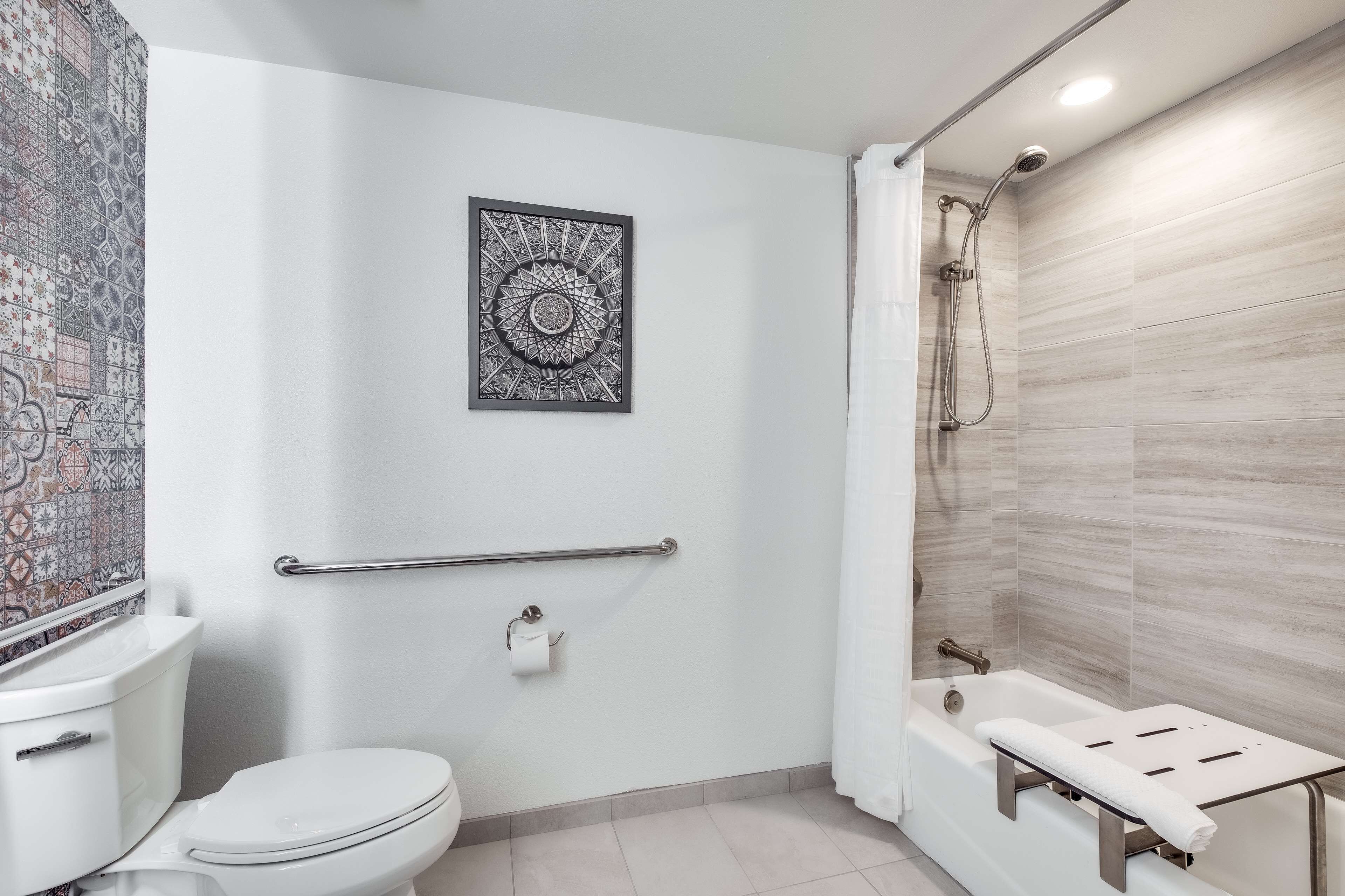 A bathroom with a toilet, a shower, a towel rack, and a patterned wall decoration.