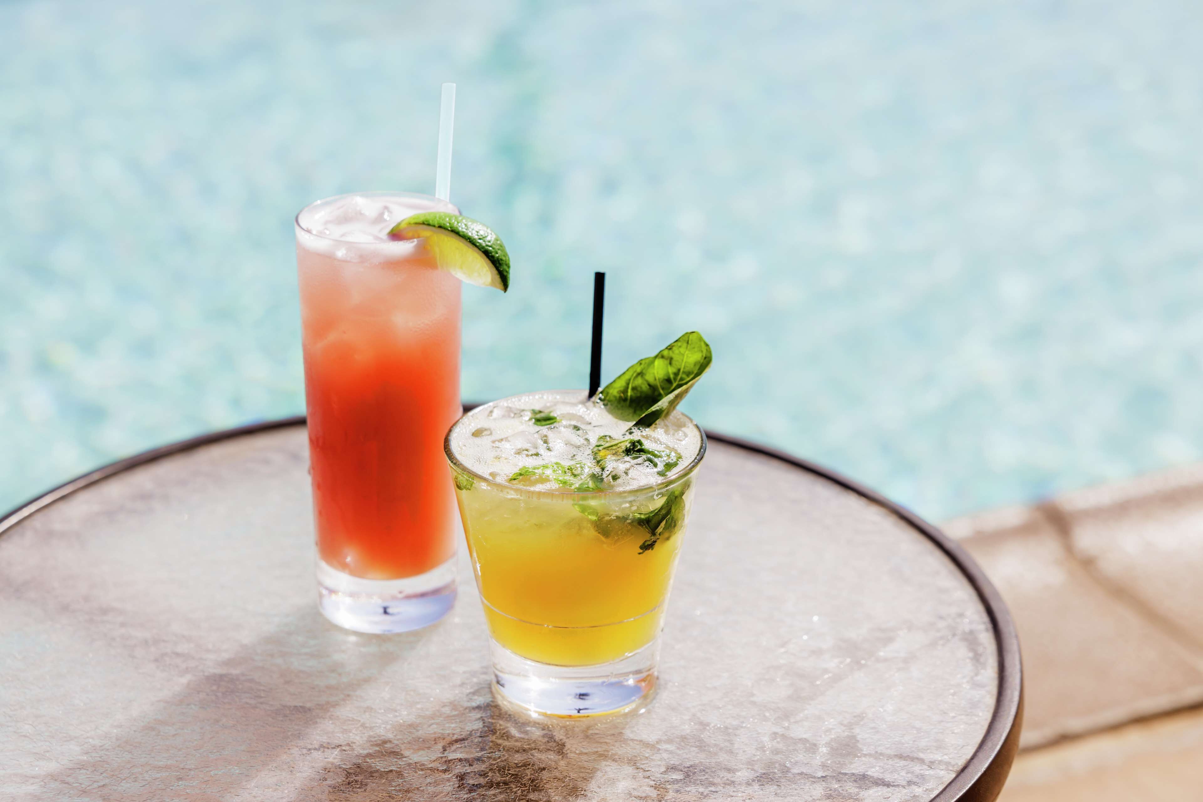Two drinks on a table by a poolside.