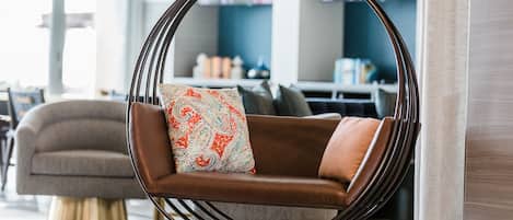 Un área de estar moderna con un sofá de cuero marrón, un sillón colgante con un cojín estampado y un televisor al fondo.
