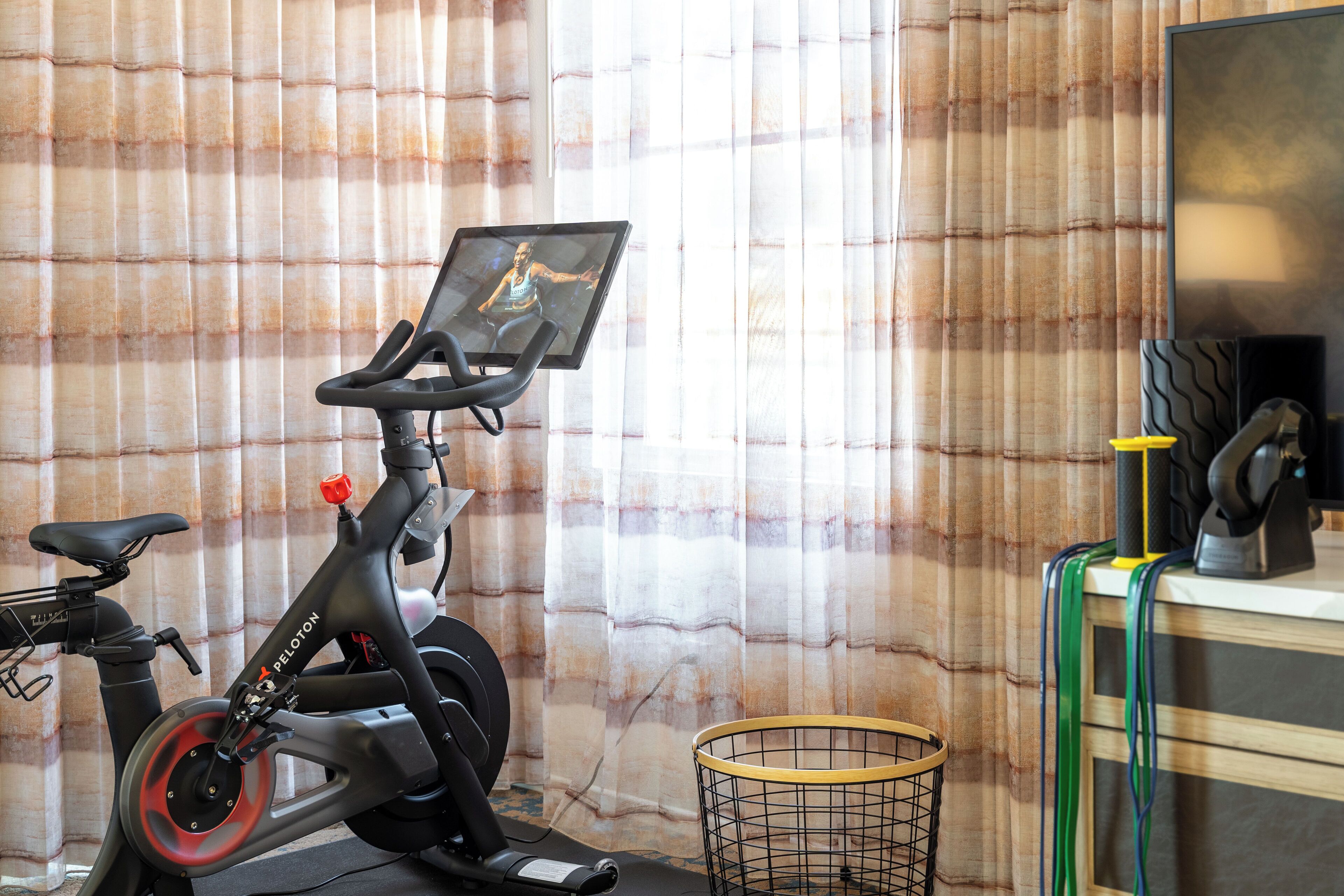 A stationary bike with a screen, a chair, and a basket in a room with curtains.