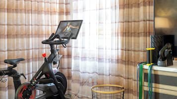 Una bicicleta estática con pantalla, una silla y una cesta en una habitación con cortinas.