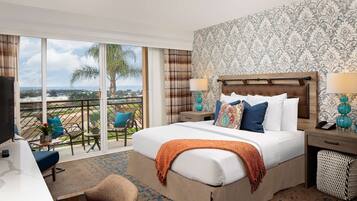 A hotel room with a large bed, a desk, a chair, a balcony with a view, and a patterned wall.