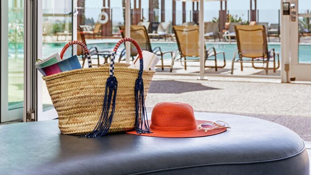 A poolside area with lounge chairs, a wicker basket, and a red hat on a cushioned bench. - The Cassara Carlsbad, Tapestry Collection by Hilton (Carlsbad)