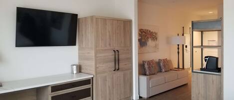 Una habitación de hotel moderna con televisión de pantalla plana, un armario de madera, un sofá y un escritorio pequeño con cajones.