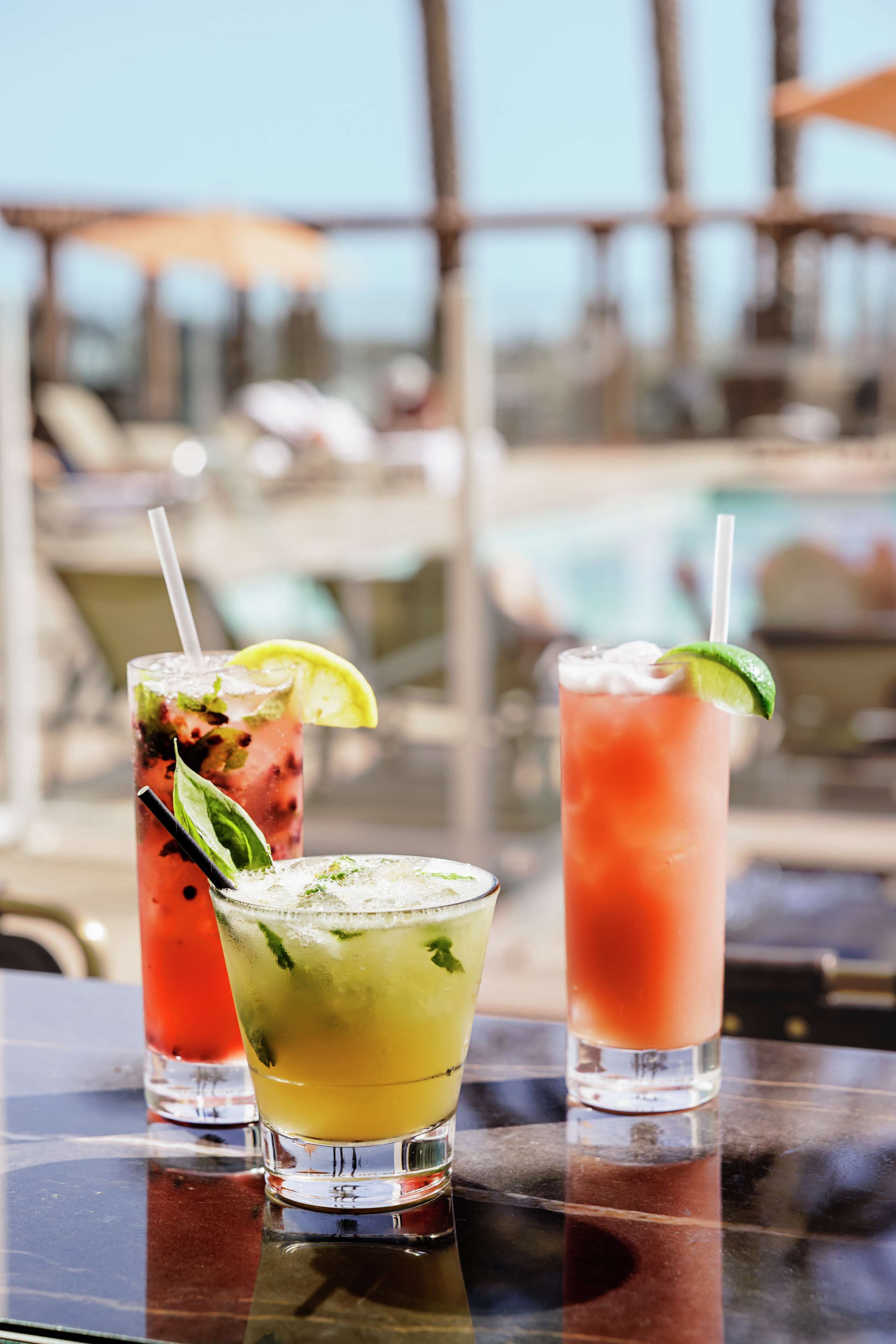 Three cocktails on a table with a pool view in the background.