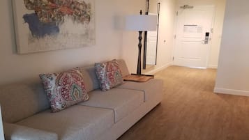 A living room with a sofa, patterned cushions, a floor lamp, and a painting on the wall.