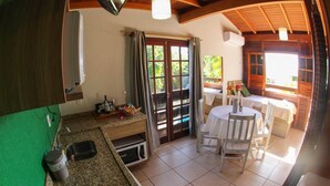 A kitchen with a sink, microwave, and a dining area with a table and chairs. - Kalani Pousada (Imbituba)