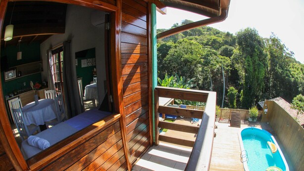 A wooden deck with a pool, a small table, and a chair. - Kalani Pousada (Imbituba)