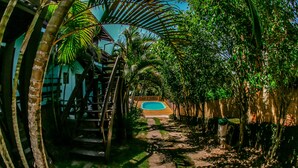 A pathway leading to a pool surrounded by lush greenery and a wooden staircase. - Kalani Pousada (Imbituba)
