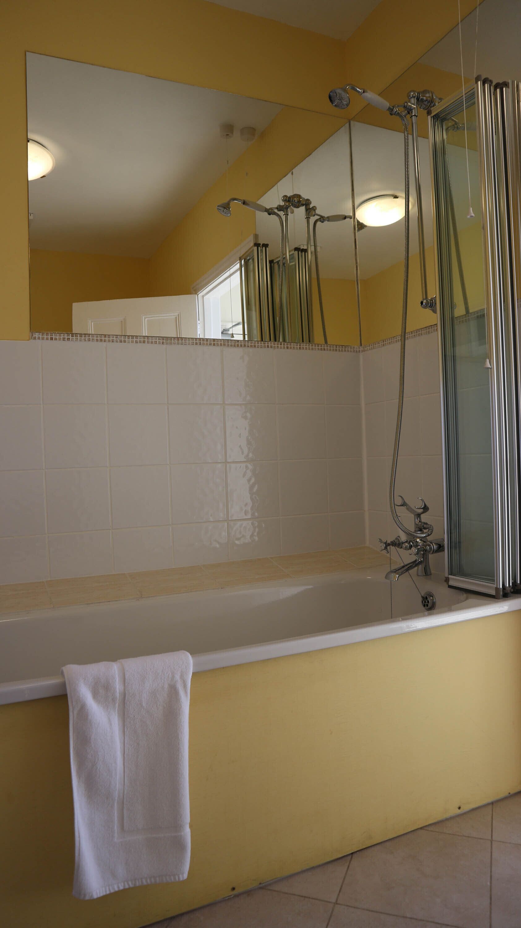 A bathroom with a bathtub, a shower, a mirror, and a towel hanging on the wall.