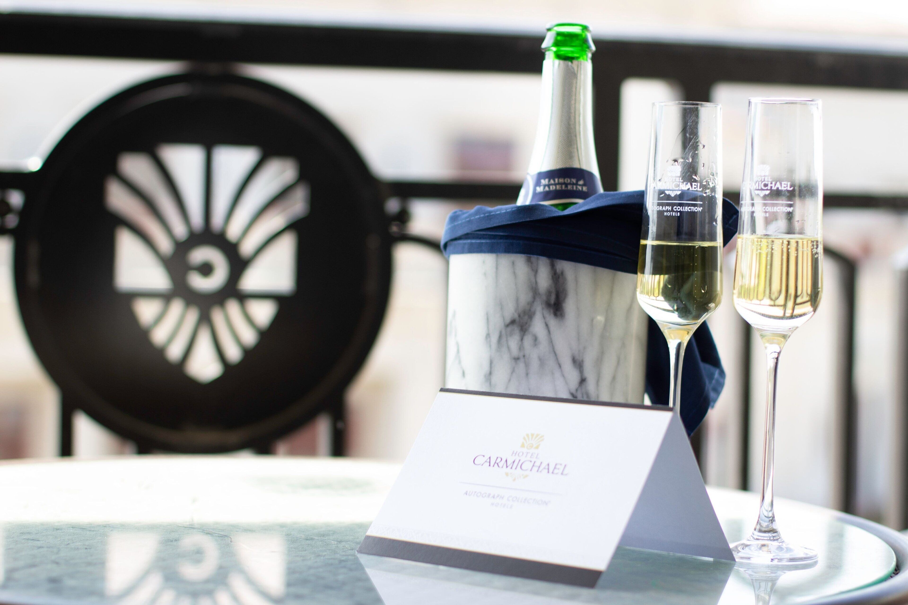 A bottle of champagne and two glasses on a table with a sign that reads "Carmichael Hotel."