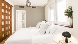 A bedroom with a bed, a hanging light fixture, a window with a view, and a wooden door. - HomeForGuest Design Attic Apartment, FREE parking (Santa Cruz de Tenerife)