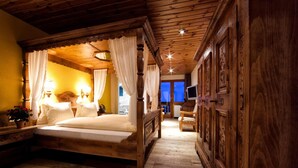 Un lit à baldaquin en bois, agrémenté de draps blancs, une table de chevet avec une lampe et une vue sur l’extérieur par une fenêtre.