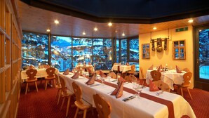 Un restaurant doté de nombreuses tables dressées pour le service, de grandes fenêtres offrant une vue sur un paysage enneigé et d’une décoration intérieure en bois.