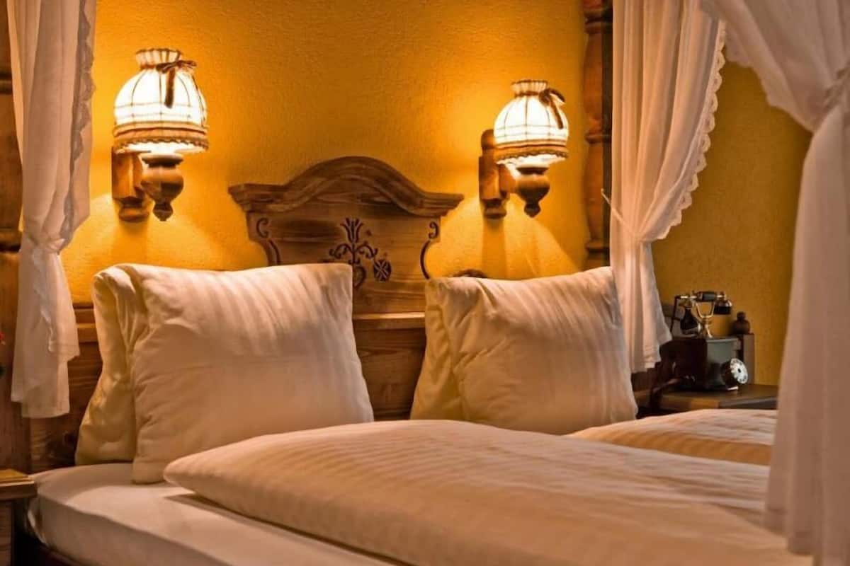 Un lit avec du linge de lit blanc, deux lampes fixées au mur et une tête de lit en bois.