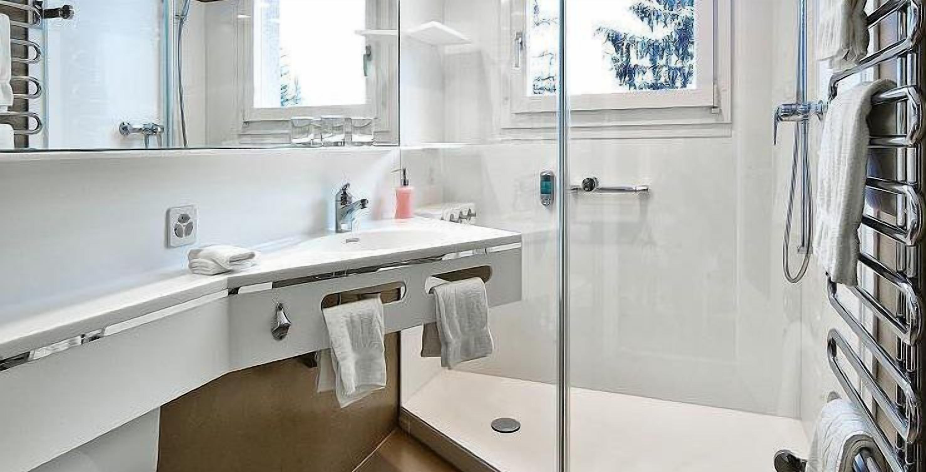 Un baño moderno con cabina de ducha de vidrio, un lavabo blanco con espejo y un perchero para toallas.