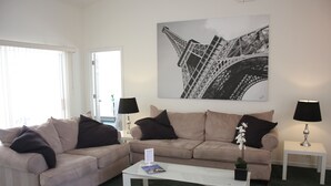 Un salon avec un canapé beige, une table basse blanche et un tableau en noir et blanc représentant un pont.