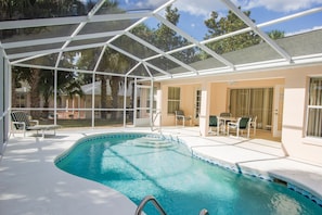 A covered swimming pool with a glass ceiling, lounge chairs, and a patio area.