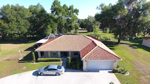 A single-story house with a red-tiled roof, a covered garage, and a driveway with a parked car.