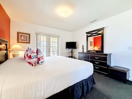 Habitación de hotel con una cama grande, televisión, cómoda y espejo.