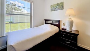 A single bed with a headboard, a bedside table with a lamp, and a painting on the wall.