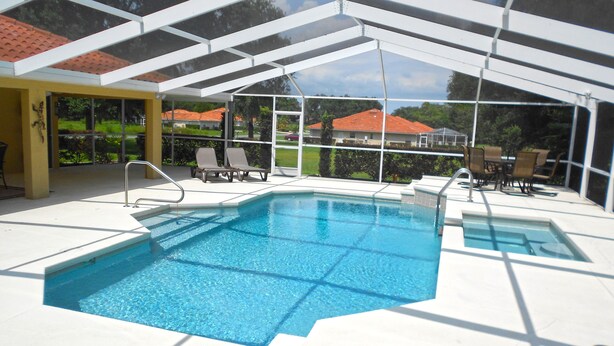 A covered outdoor swimming pool with lounge chairs and a view of houses in the background.