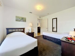 Habitación de hotel con dos camas, una mesita de noche con lámpara, un aparador con un coche de juguete y un cuadro en la pared.