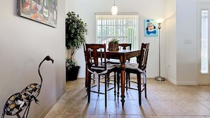A dining area with a table and chairs, a potted plant, and a painting on the wall.
