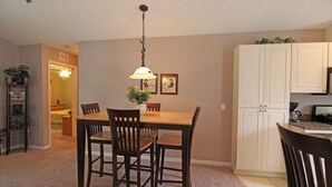 Uma área de refeições com mesa e cadeiras de madeira, luminária pendente e cozinha com armários brancos.