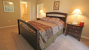 Quarto com uma cama, mesas de cabeceira, cômoda e porta que dá para outro espaço.