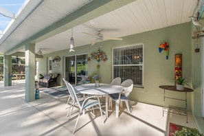 Un patio cubierto con una mesa y sillas para comer, un ventilador de techo y decoración en las paredes.