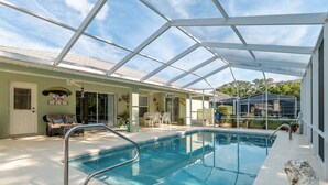 A covered swimming pool with a glass ceiling, a lounge area with chairs and a sofa, and a door with a 'No Diving' sign.