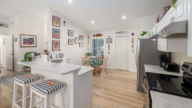 A modern kitchen with a central island, bar stools, a dining area with a table and chairs, and a refrigerator.